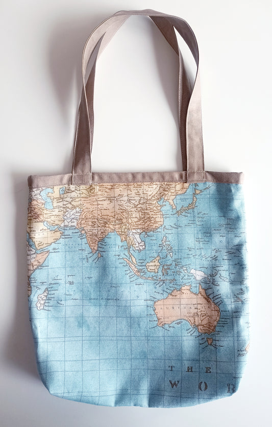 Υφασμάτινη τσάντα ώμου με ύφασμα vintage σχέδιο του παγκόσμιου
χάρτη σε γαλάζιο φόντο και αποχρώσεις του μπεζ. Υπάρχει μια μπεζ ρίγα στο πάνω μέρος και τα χερούλια είναι από το ίδιο μπεζ ύφασμα.