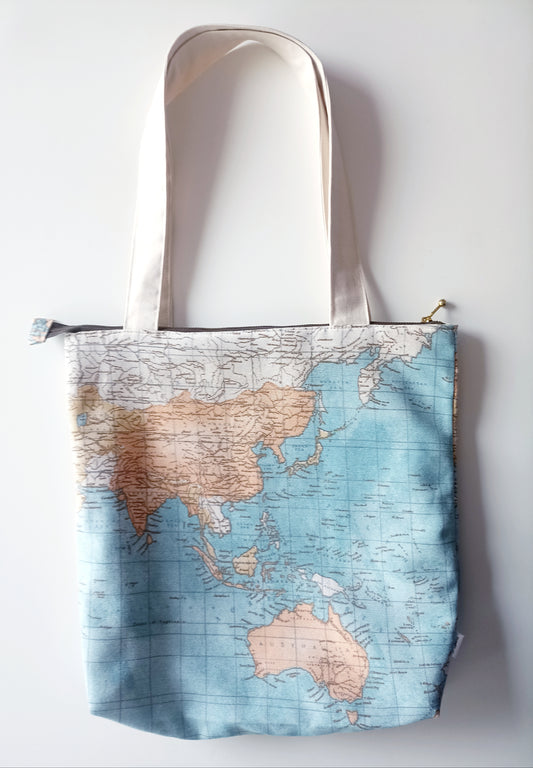 Υφασμάτινη τσάντα ώμου με ύφασμα vintage σχέδιο του παγκόσμιου
χάρτη σε γαλάζιο φόντο και αποχρώσεις του μπεζ. Τα χερούλια είναι από εκρού ύφασμα καμβά. Υπάρχει χρυσό μεταλλικό φερμουάρ με καφέ ύφασμα.