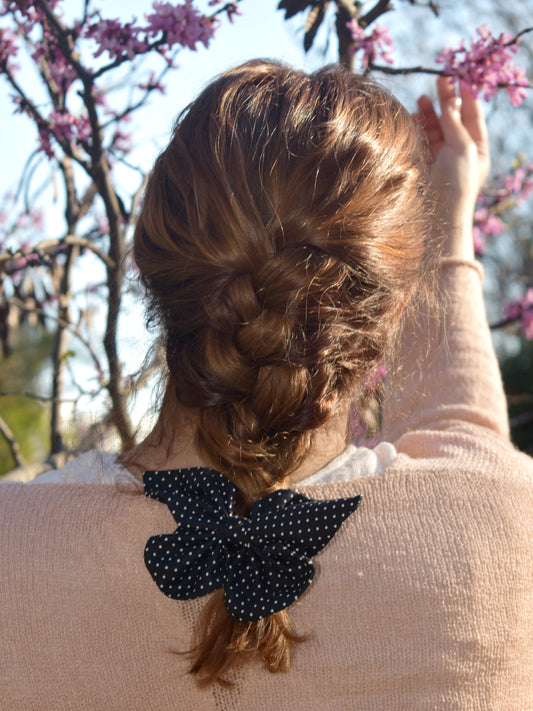 Υφασμάτινη μαύρη πεταλούδα με μικρά λευκά πουα, φορεμένη σε καστανοκόκκινα μαλλιά 