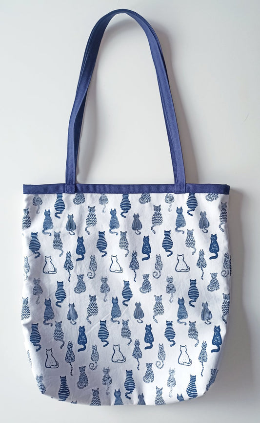 Υφασμάτινη τσάντα ώμου απο λευκό ύφασμα και μπλε τελείωμα,
με σχέδιο σώματα - πλάτες γατών σε ριγέ, πουά , ζικζακ μπλε - λευκό χρώμα.